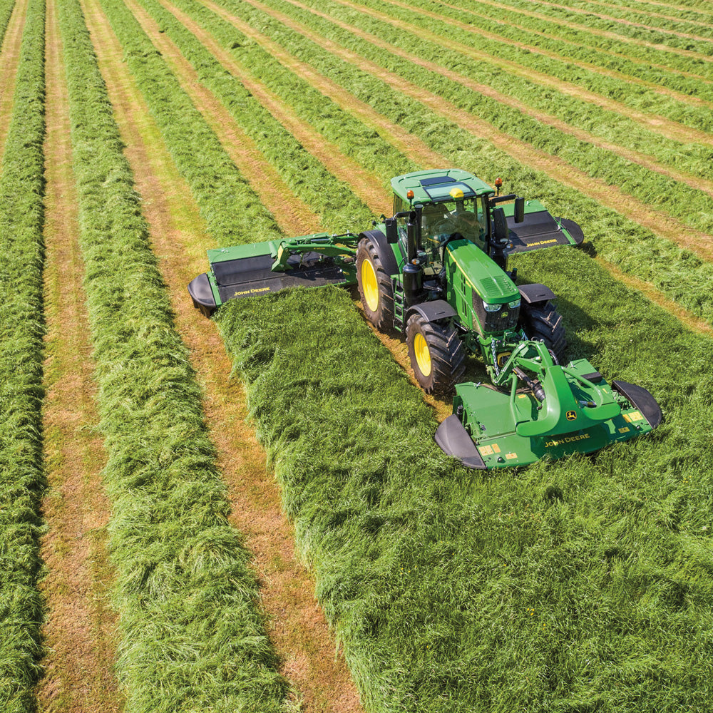 Green tractor mowing a field with rows of cut grass.